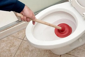 Plumber unclogging a toilet with a plunger
